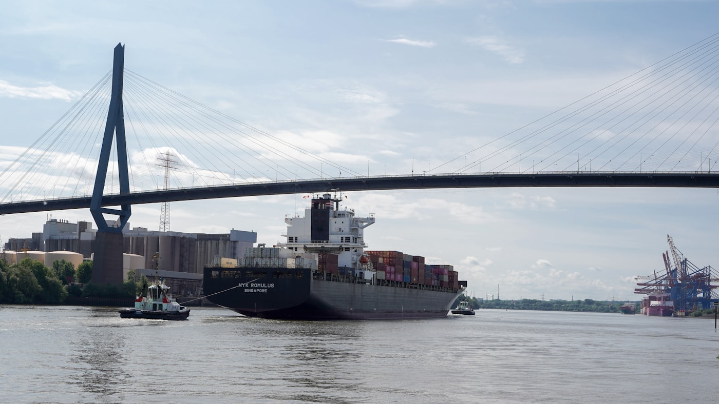 A large container ship entering a harbor beneath a bridge